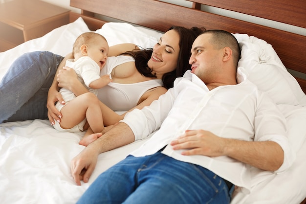 Happy young family of mother father and little baby woman smiling rejoicing lying on bed at home.