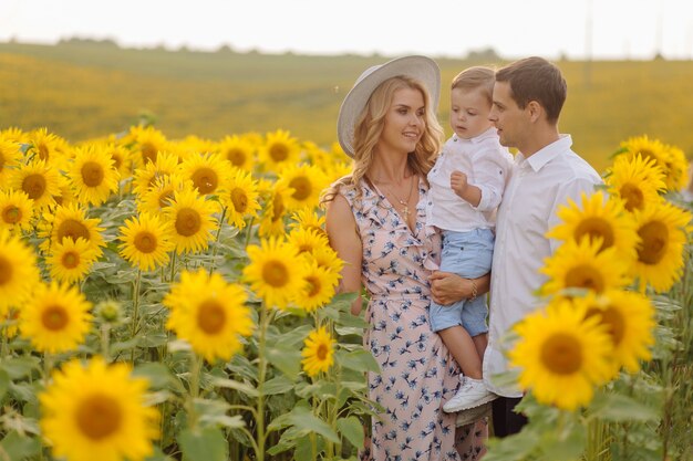 Happy young family, mother father and son, are smiling, holding and hugging in the sunflower field