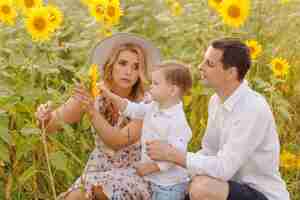 Free photo happy young family, mother father and son, are smiling, holding and hugging in the sunflower field