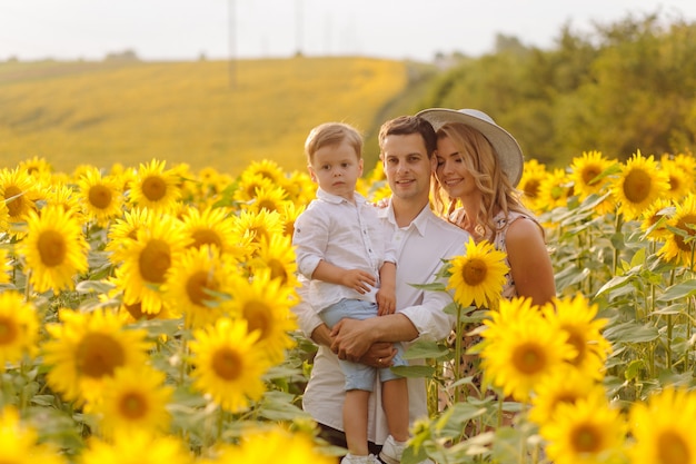 Счастливая молодая семья, мать отца и сына, улыбаются, держатся и обнимаются в поле подсолнечника