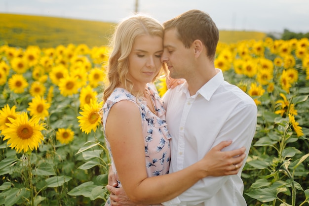 Happy young family, mother father and son, are smiling, holding and hugging in the sunflower field