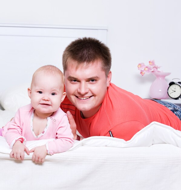 Felice giovane padre con bambino sorridente sdraiato sul letto in camera da letto