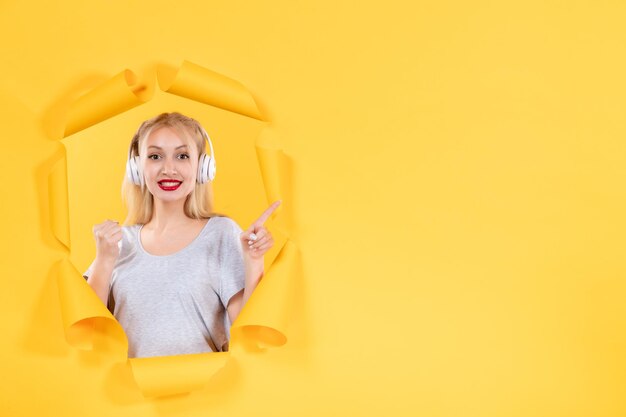 Happy young female in headphones on torn yellow paper background ultrasound music audio sound