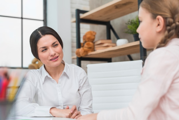 Happy young female psychologist looking at girl in the office