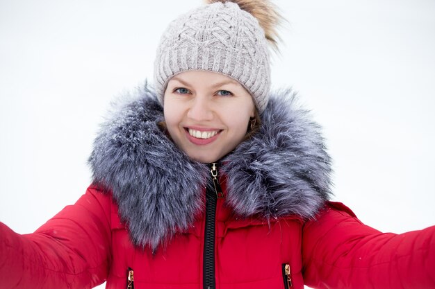 屋外の肖像画を撮っている赤い冬のジャケットの幸せな若い女性