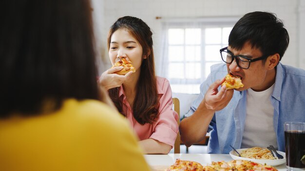 집에서 점심을 먹고 행복 젊은 친구 그룹입니다. 아시아 가족 파티 피자 음식을 먹고 집에서 함께 식탁에 앉아있는 동안 식사를 즐기고 웃고. 축하 휴가 및 공생.