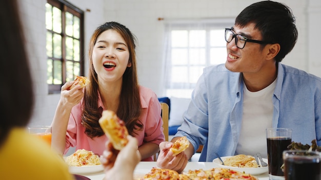 Группа счастливых молодых друзей обедает дома. Азиатская семейная вечеринка ест пиццу и смеется, наслаждаясь едой, сидя за обеденным столом вместе дома. Праздник праздника и единения.
