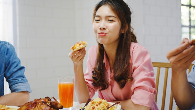 Happy young friends group having lunch at home. Asia family party eating pizza food and laughing enjoying meal while sitting at dining table together at house. Celebration holiday and togetherness.