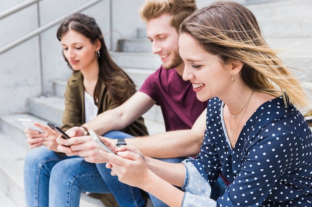 Free photo happy young friends sitting on staircase using cellphone