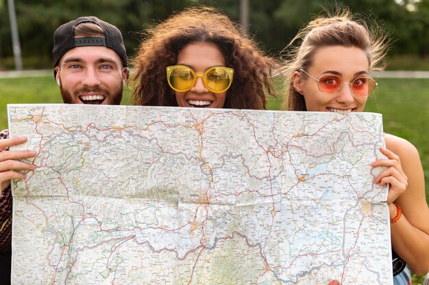 Happy young funny company of friends tourists hiding behind map in sunglasses, man and women having fun together, traveling