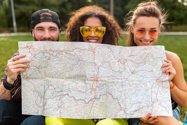 Happy young funny company of friends tourists hiding behind map in sunglasses, man and women having fun together, traveling
