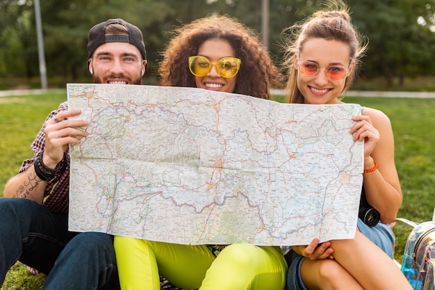 Happy young funny company of friends tourists hiding behind map in sunglasses, man and women having fun together, traveling