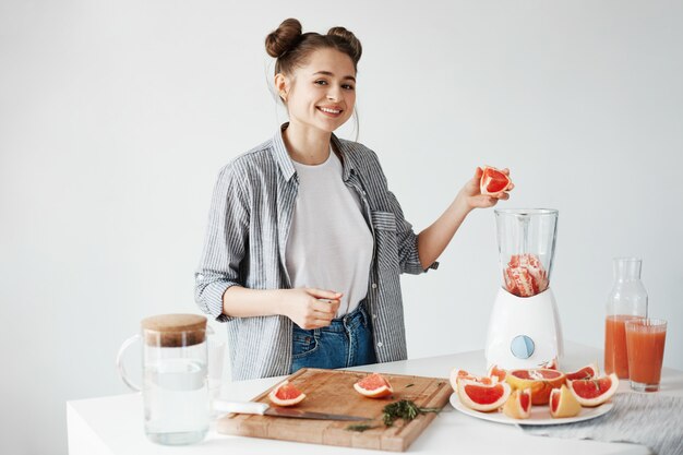 Happy young girl blending healthy detox fresh grapefruit smoothie over white wall.