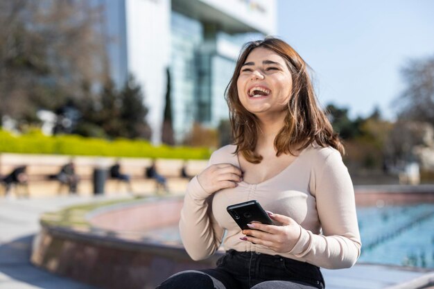 Happy young girl holding her phone and laughing High quality photo