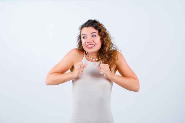 Happy young girl is looking left and holding fists on chest on white background