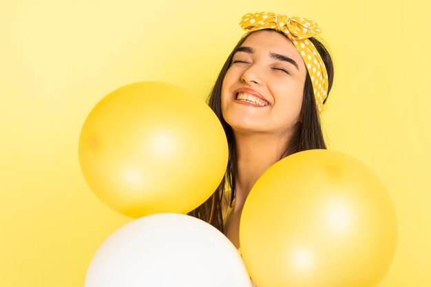 笑って、黄色の背景に風船を保持している幸せな少女高品質の写真