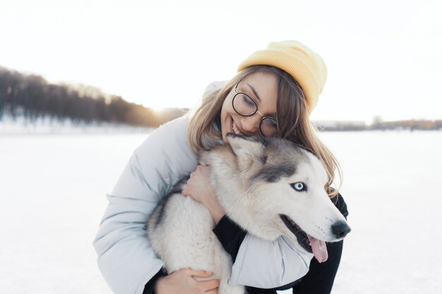 冬の公園でシベリアンハスキー犬と遊んで幸せな若い女の子