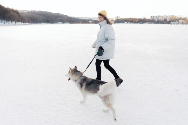 Счастливая маленькая девочка играя с собакой сибирской лайки в парке зимы