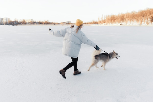 冬の公園でシベリアンハスキー犬と遊んで幸せな若い女の子