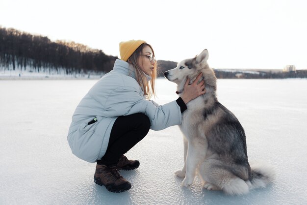 冬の公園でシベリアンハスキー犬と遊んで幸せな若い女の子