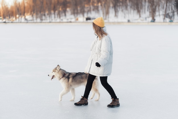 冬の公園でシベリアンハスキー犬と遊んで幸せな若い女の子