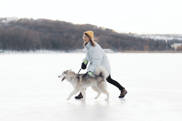 冬の公園でシベリアンハスキー犬と遊んで幸せな若い女の子