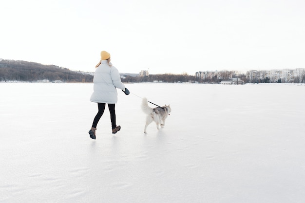 Счастливая маленькая девочка играя с собакой сибирской лайки в парке зимы