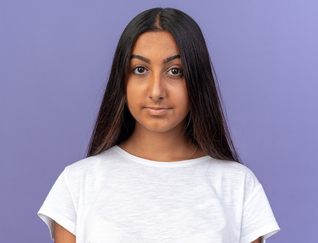 Happy young girl in white t-shirt looking at camera smiling confident standing over blue background