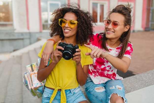 Amici di ragazze giovani felici sorridente seduto in strada con macchina fotografica, donne che si divertono insieme