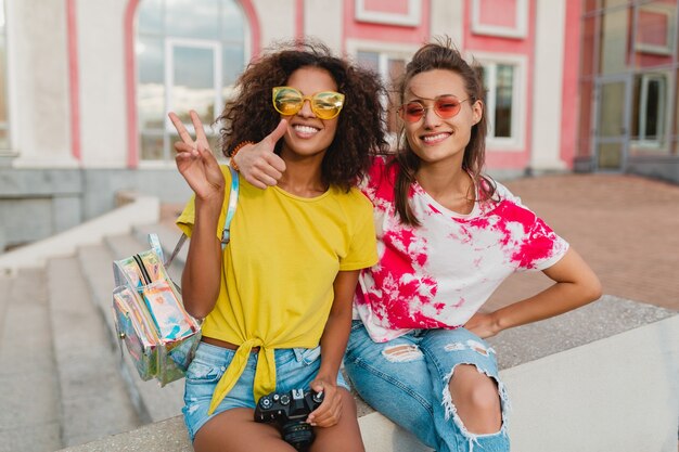 Happy young girls friends smiling sitting in street with photo camera, women having fun together