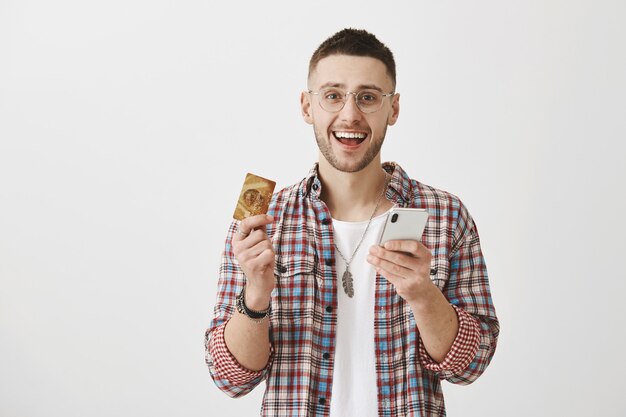 Happy young guy with glasses posing with his phone  and card