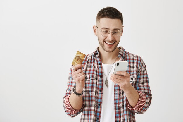 Happy young guy with glasses posing with his phone  and card