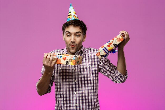 Happy young handsome man opening birthday gift over purple wall.