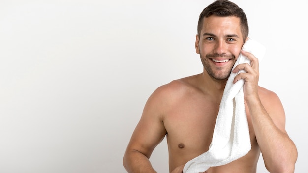 Foto gratuita giovane uomo bello felice con l'asciugamano bianco sopra la parete bianca
