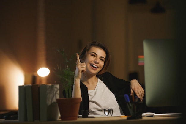 Happy young lady designer sitting in office at night
