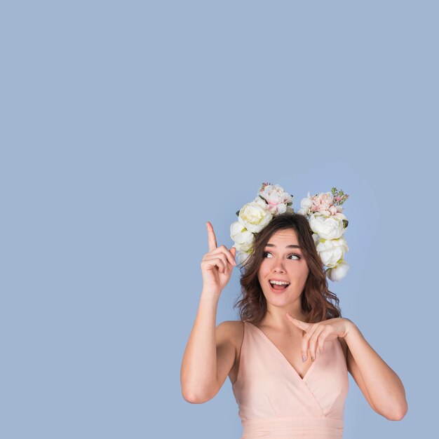 Happy young lady in dress with flower wreath pointing upstairs