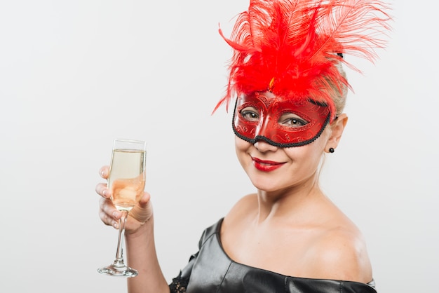 Happy young lady in mask with red feathers holding glass