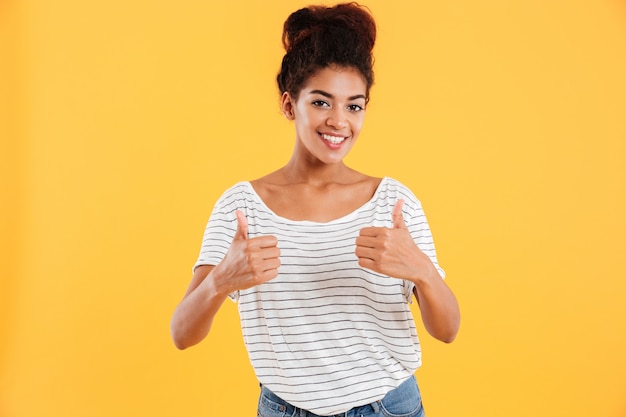 Happy young lady showing thumbs up and smiling isolated over yellow