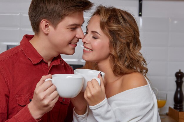 Happy young lovely couple on kitchen hugging each other. They enjoy spending time togehter. They drink coffee and smiling