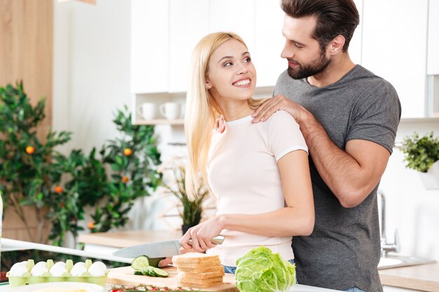 Happy young loving couple standing at kitchen and cooking