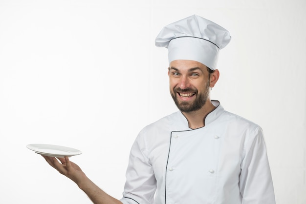 Happy young male chef holding an empty white plate against white backdrop