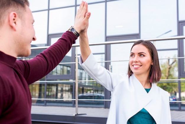 Happy young male and female friend giving high five at outside