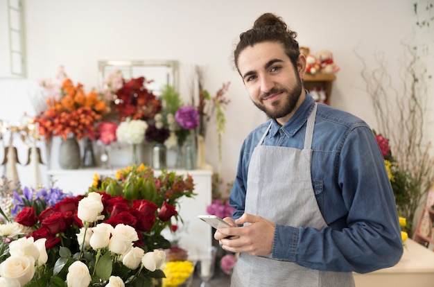 Happy young male florist holding mobile phone in hand looking to camera