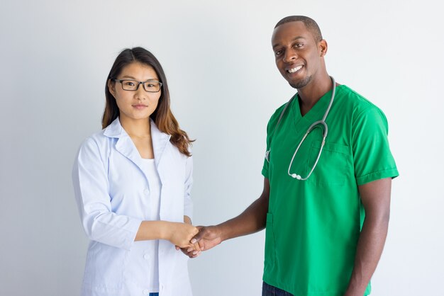Happy young male physician and female doctor shaking hands.