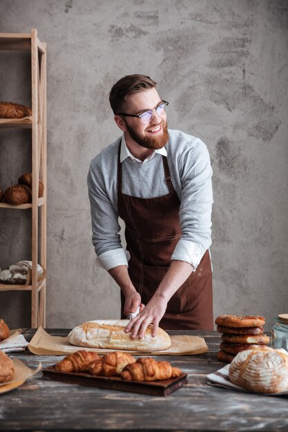 빵집에서 행복 한 젊은 남자 베이커 서 빵을 잘라.