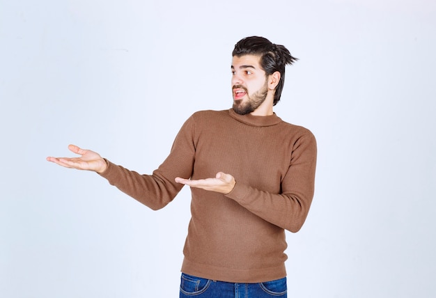 Free photo a happy young man in brown sweater standing and showing something with hands.