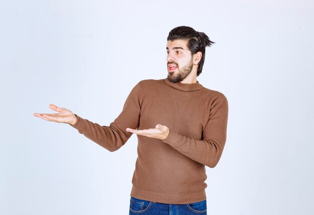 A happy young man in brown sweater standing and showing something with hands.