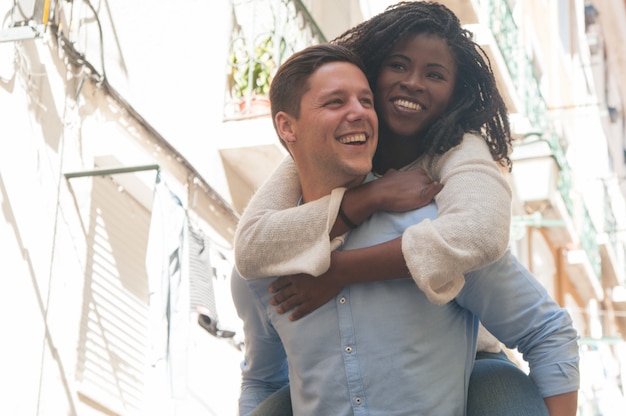 Happy young man carrying girlfriend on back outdoors