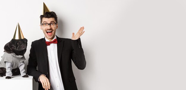 Happy young man and cute black dog wearing party cones celebrating birthday guy friendly saying hell