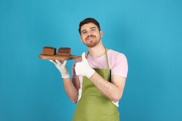 Happy young man holding chocolate cake slices on a blue.